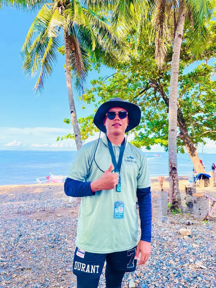 Staff member standing under palm trees near the beach